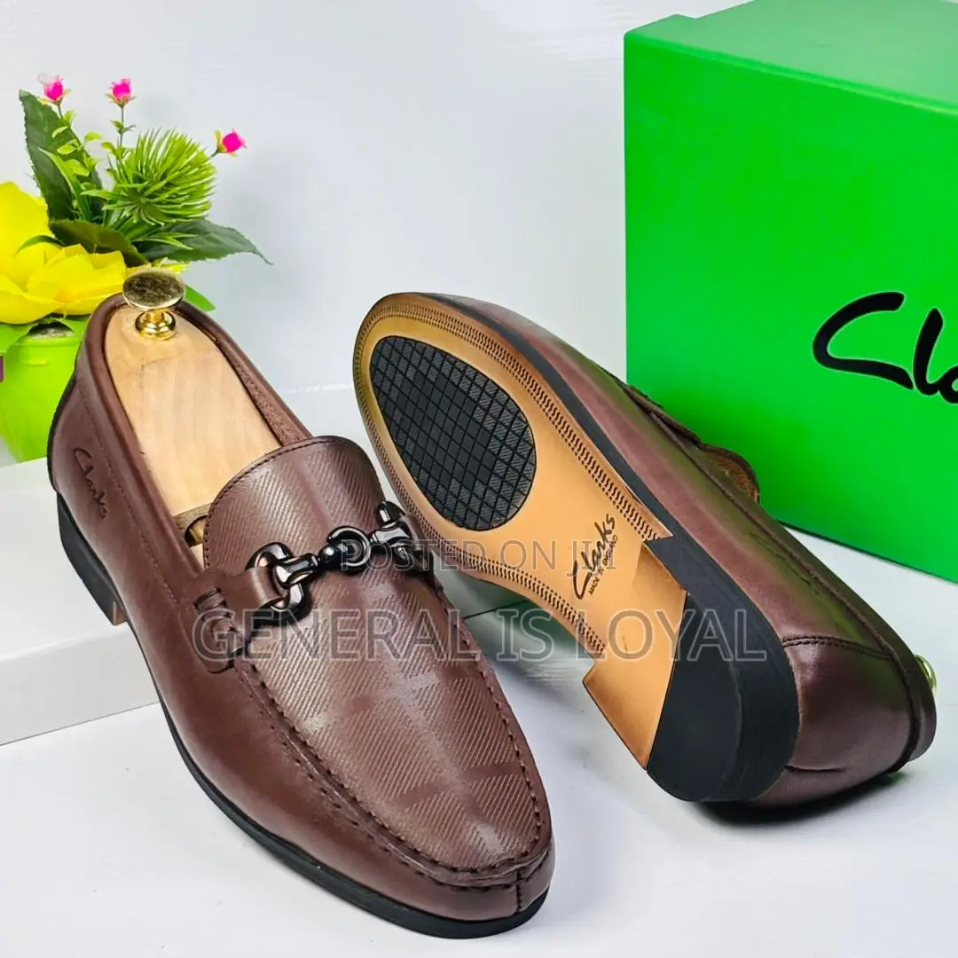 Brown Clarks Loafers With A Metal Buckle And Patterned Leather.
